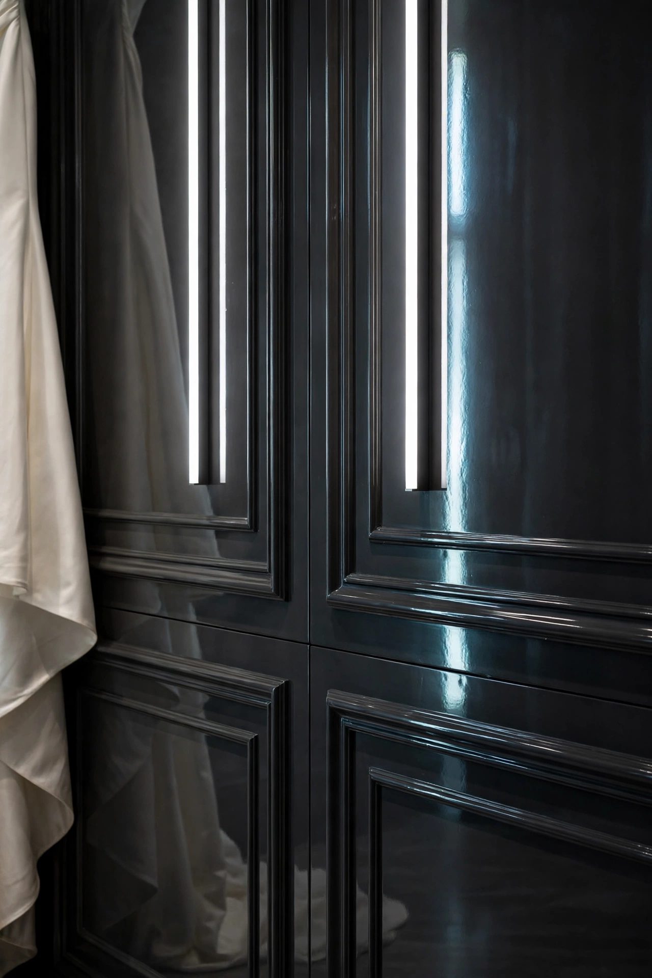 Vertical light strips reflected in long streaks down a deep charcoal mirror-gloss paneled wall, beside a satin gown