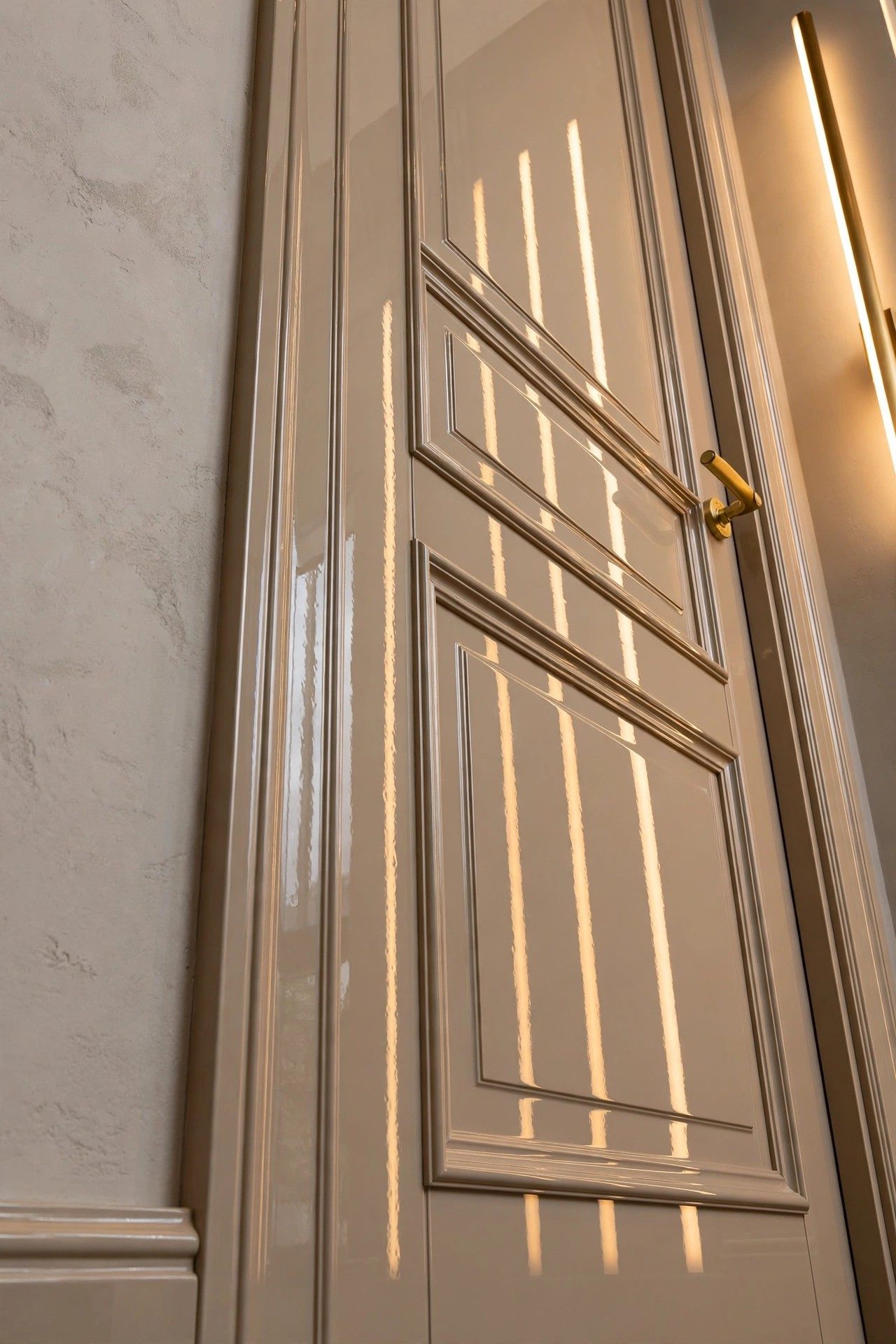 A paneled door and trim in champagne-ivory high-gloss lacquer, crisp edges reflecting vertical light